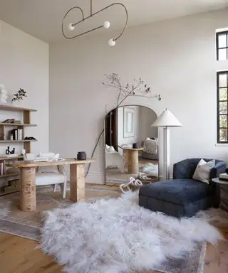 Grand miroir de sol dans un salon ouvert et un espace bureau avec tapis à poils longs, lampadaire crème et chaise longue en velours bleu marine en acier