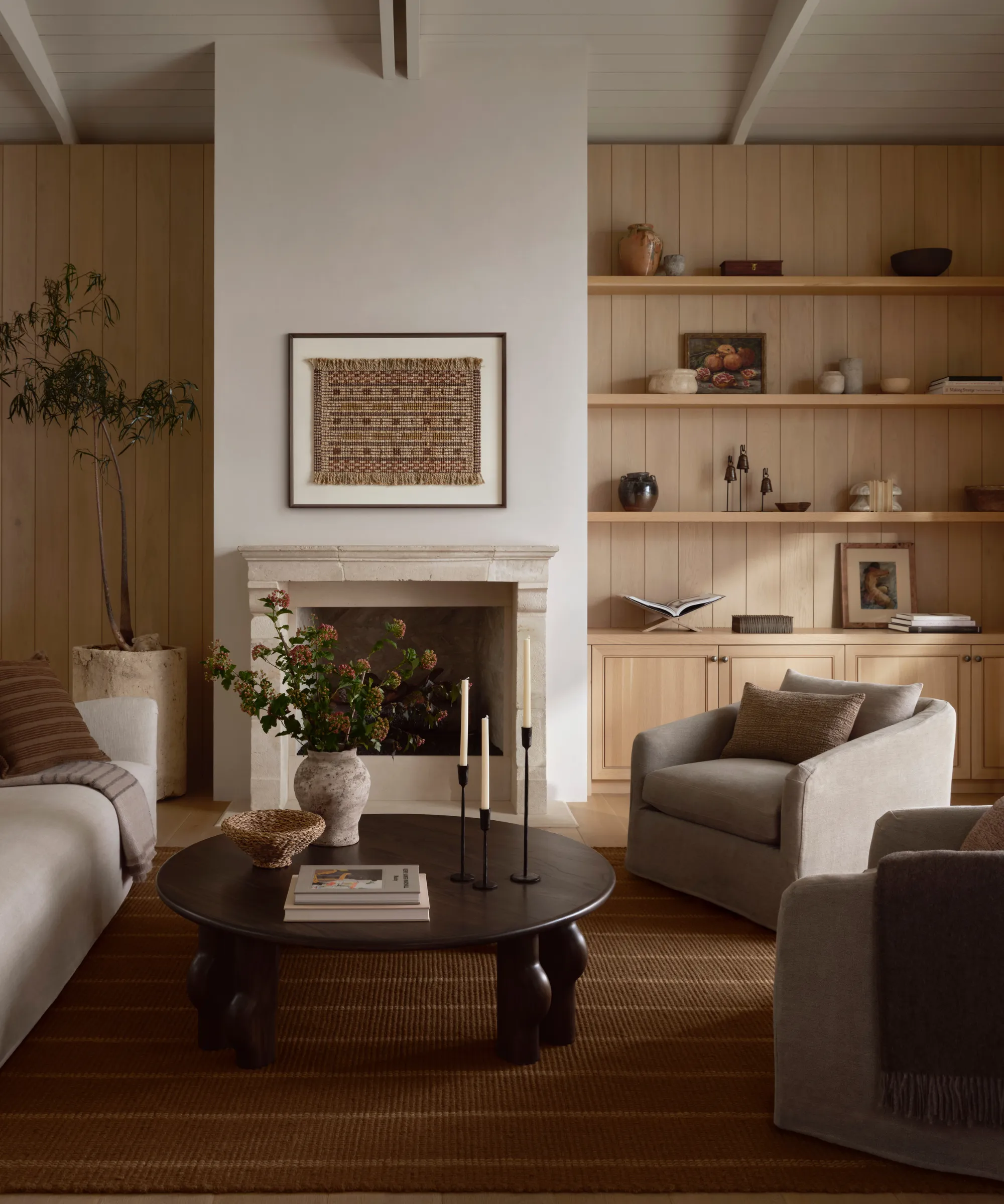 ciepły salon z boazerią na ścianach okrągły drewniany stolik kawowy dwa akcentowane krzesła kanapa i dywanik w paski na ziemi' loading='lazy' title=