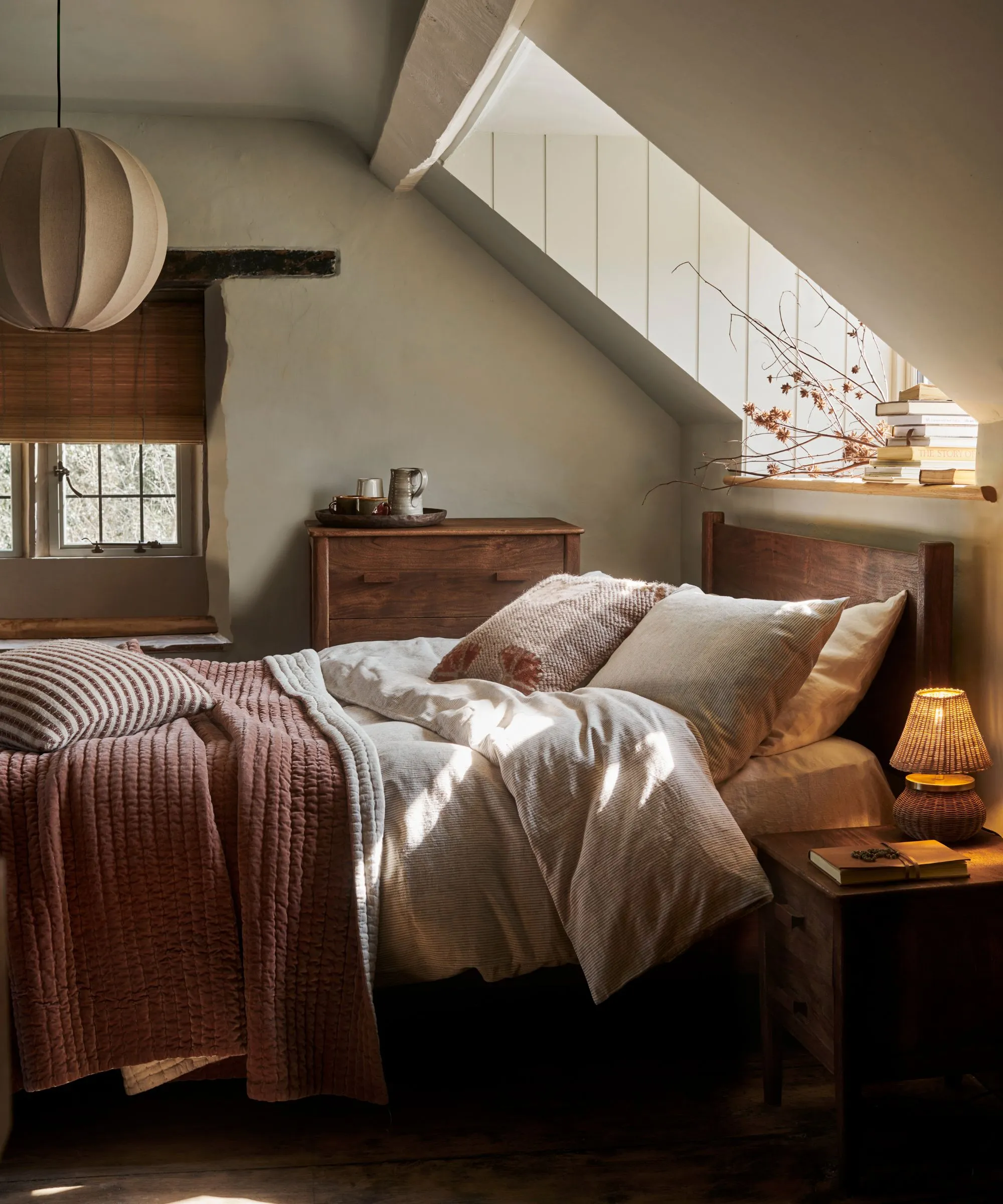 Et hyggeligt soveværelse med efterår med en træbamme og neutral sengetøj. Et skråt tag med et ovenlysvindue over.' loading='lazy' title=