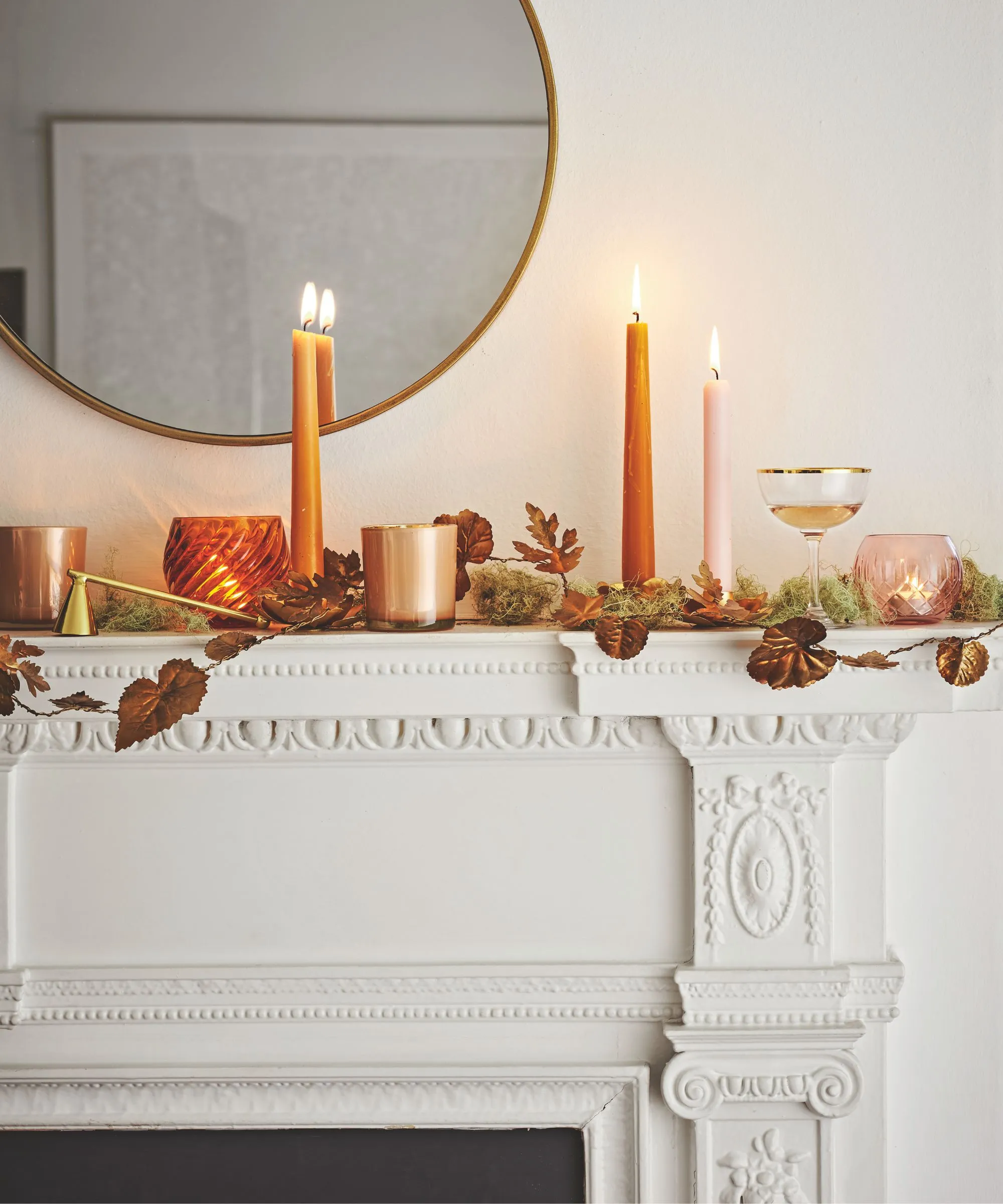 En hvid høstlig pejs med blade stearinlys og et cirkulært spejl ovenfor' loading='lazy' title=