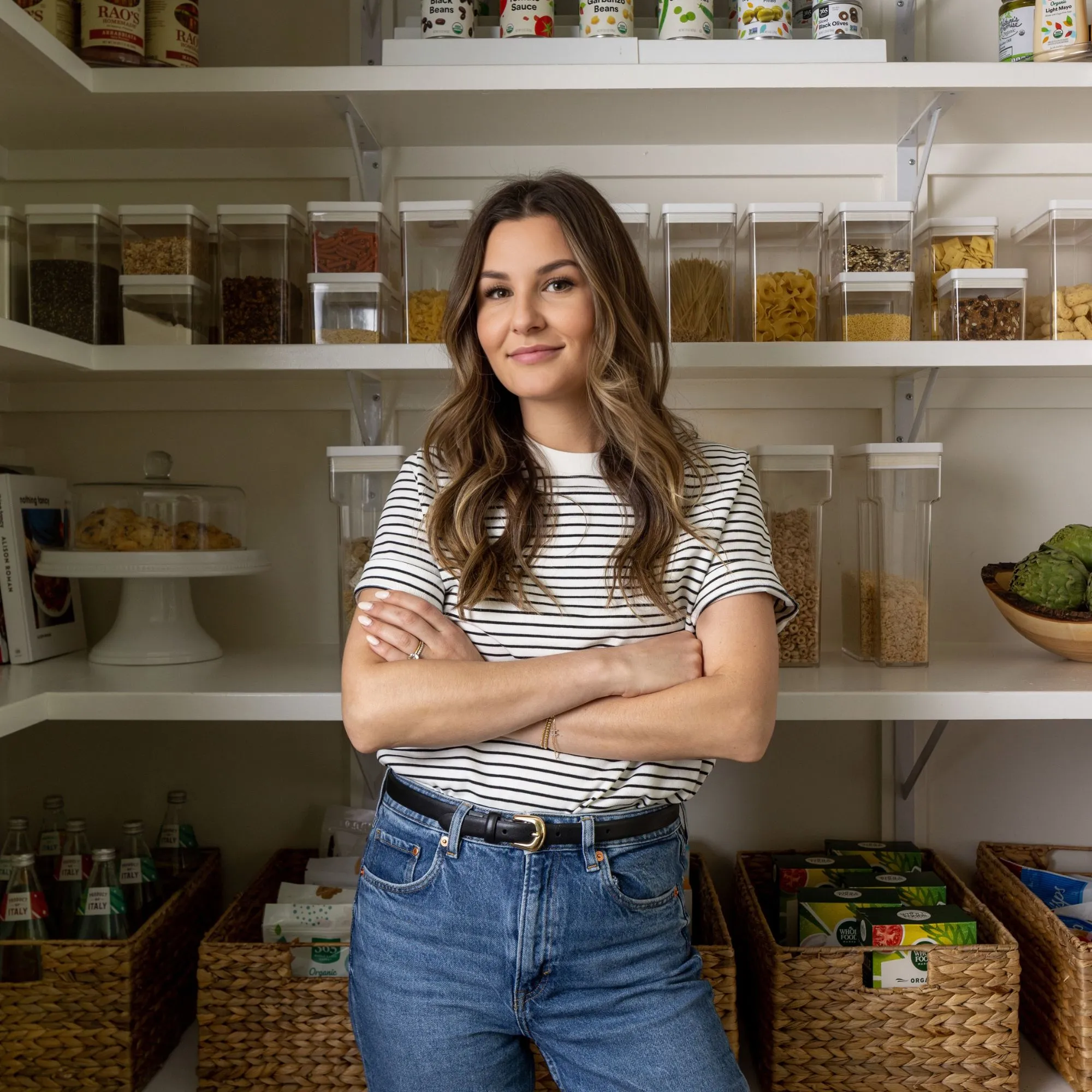 Ein Bild von Ashley La Fond, die ein T-Shirt und Jeans trägt und in einer Speisekammer steht, mit Ajrs und Dosen hinter ihr.' loading='lazy' title=