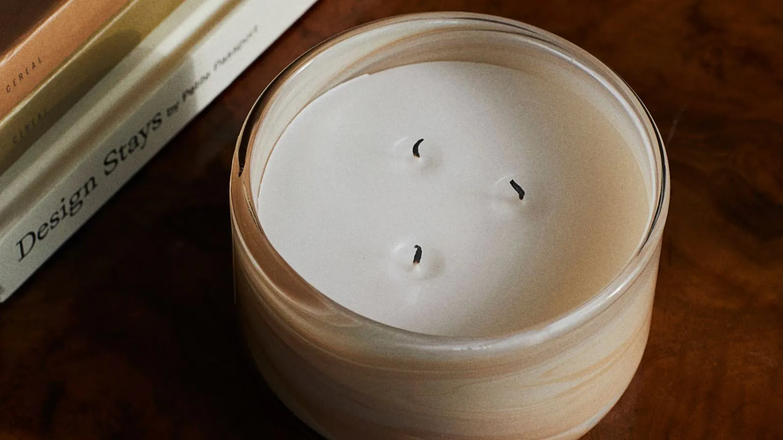 Świeca z trzema knotami i kremową, wirującą szklaną oprawką na mahoniowym stoliku kawowym' loading='lazy' title=