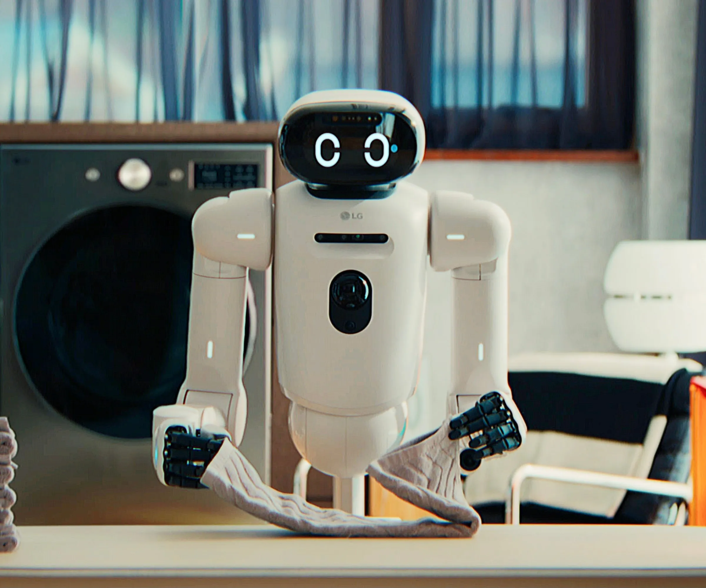 Składany ręcznik robota LG CLOiD na zdjęciu przed pralką.' loading='lazy' title=