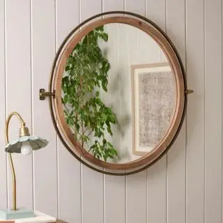 Et rundt speil på en hvit trevegg med en lampe til venstre