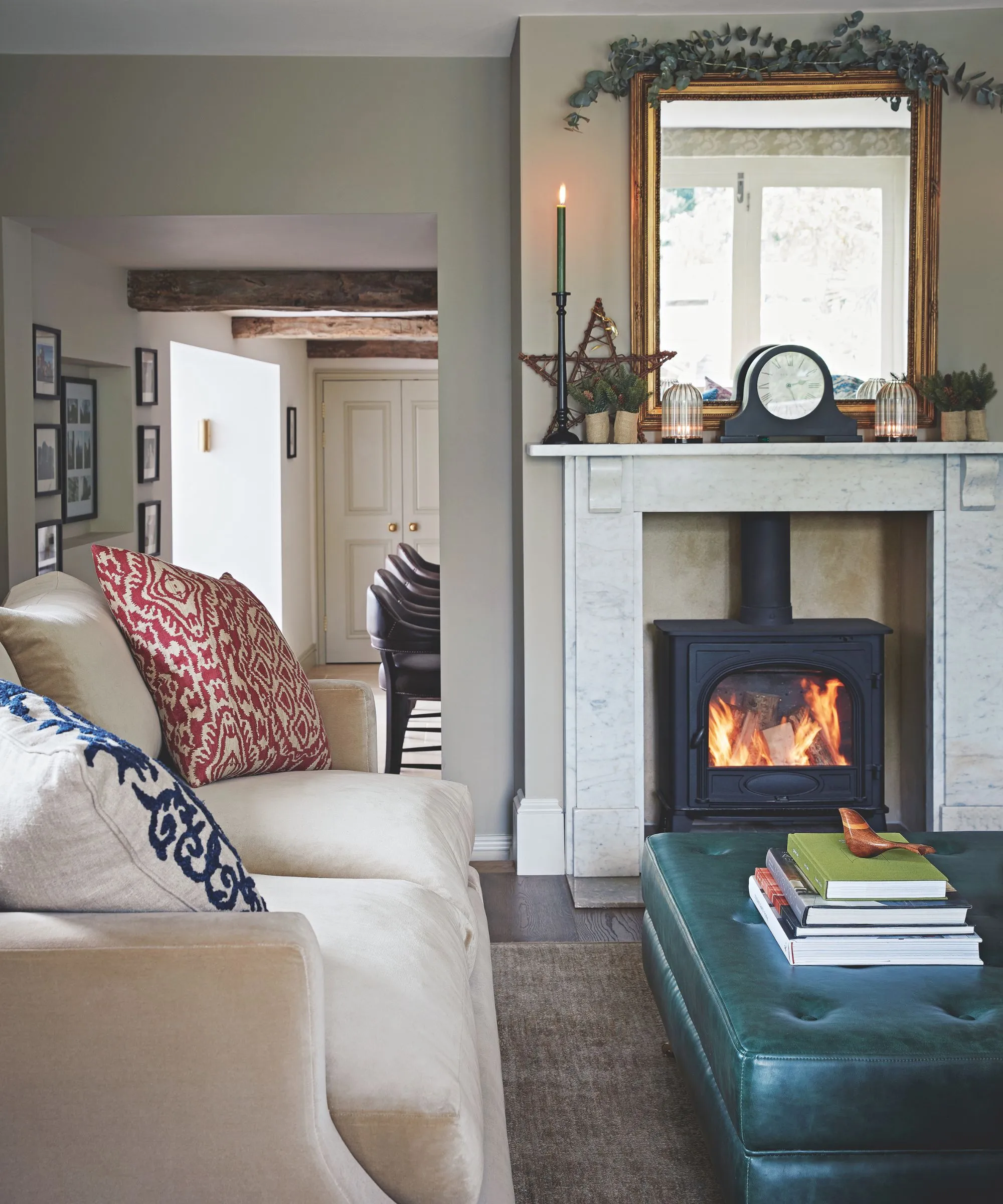 Un accogliente soggiorno con un bruciatore a legna illuminato, una candela bianca, un divano con cuscini fantasia, un pouf in pelle e una mensola in marmo con un orologio decorativo e uno specchio sulla parte superiore.' loading='lazy' title=