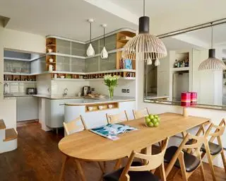 Une cuisine ouverte blanche avec table en bois, chaises et suspension.