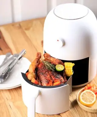 Une friteuse à air blanche sur un comptoir de cuisine avec un poulet rôti à l'intérieur