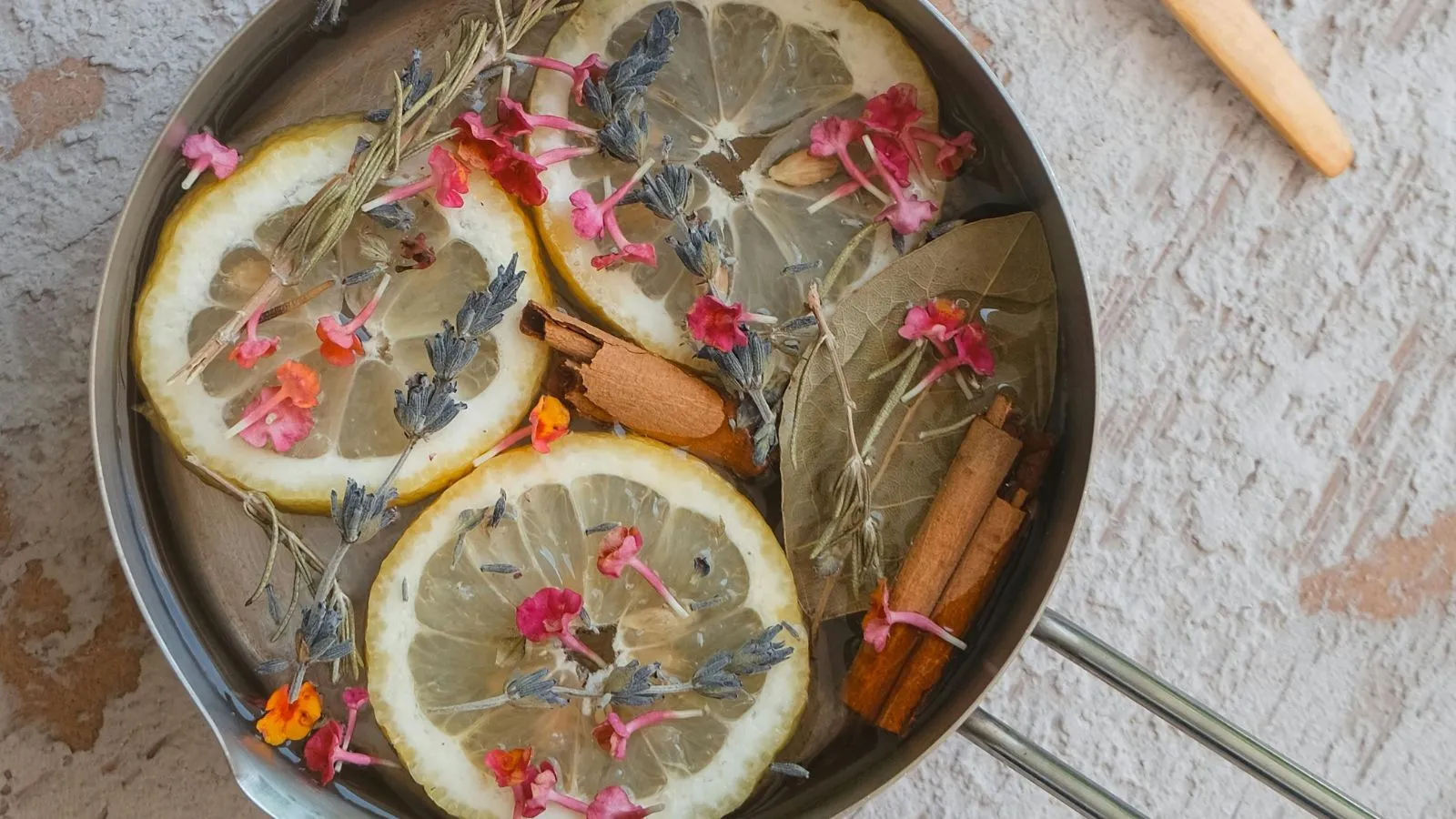 Widok z lotu ptaka na metalowy garnek wypełniony suszonymi kwiatami pokrojonymi w plasterki cytryny i laskami cynamonu' loading='lazy' title=