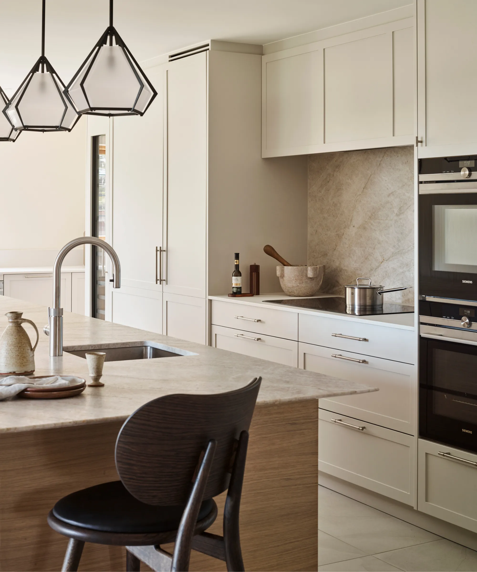 nowoczesna, minimalistyczna kuchnia z białymi szafkami i blatami. tylna ściana z kamienia naturalnego za szklaną płytą kuchenną i dopasowana kamienna wyspa' loading='lazy' title=