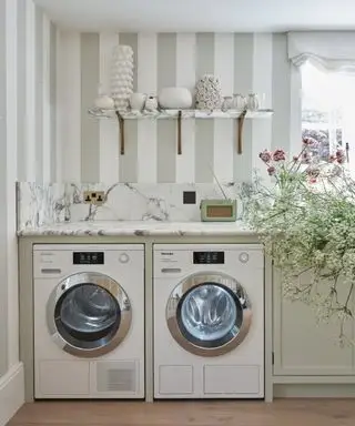 シックなファームハウス スタイルのランドリー ルームにあるミーレの洗濯機。ストライプの壁紙とシンクに花が付いています。