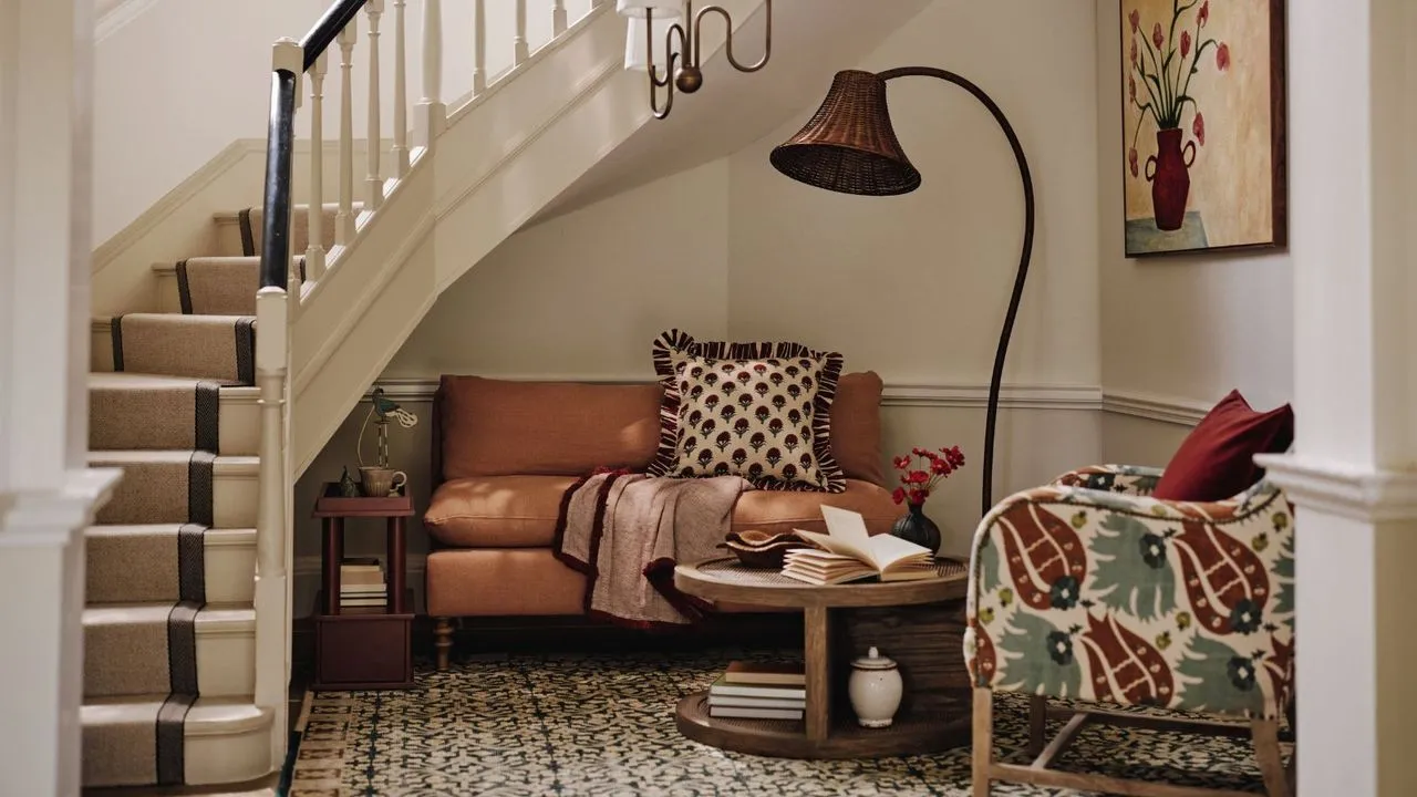 Przytulna część wypoczynkowa z małą sofą i fotelem umieszczonym pod kręconymi schodami. Obok nich duża rzeźbiona lampa i nisko wiszący wisiorek.' loading='lazy' title=
