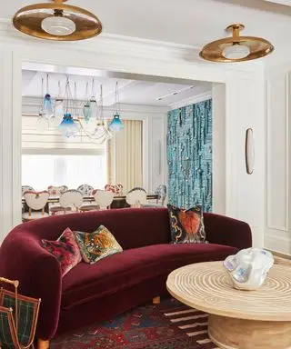 Canapé incurvé bordeaux en velours, placé sur un tapis à motifs encadrant une table basse en bois et arrondie