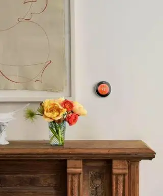 Un petit thermostat intelligent orange sur un mur beige au-dessus d'un côté marron avec des fleurs rouges et jaunes